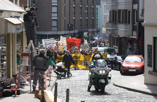 The demonstration, escorted by a police motorcycle and two police officers in front, ascends the hill towards Aachen’s historic market place.