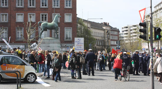 Eine Menschenmenge auf dem Aachener Theaterplatz, inklusive einiger Polizisten und einiger Schilder mit Aufschriften wie &ldquot;MIt Studiengebühren sanieren wir die Hochschule&rdquot;