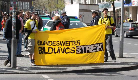 Zwei Personen mit gelben T-Shirts halten ein kleineres Banner mit dem Logo des Bildungsstreiks