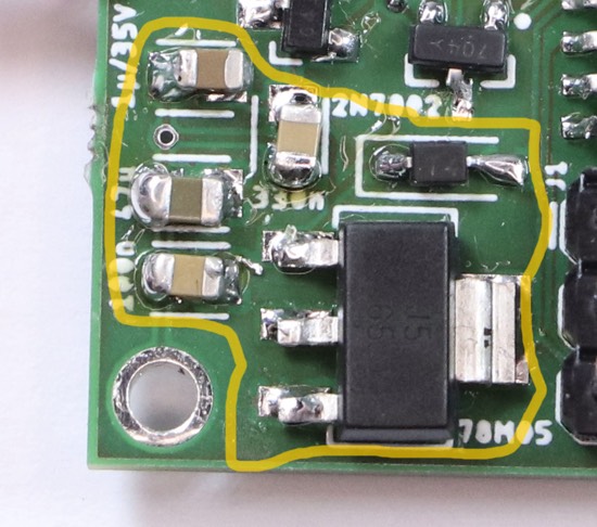 Excerpt from the photograph of the circuit board. A large piece with three pins on one side and a metal tab on the other is highlighted together with some capacitors.
